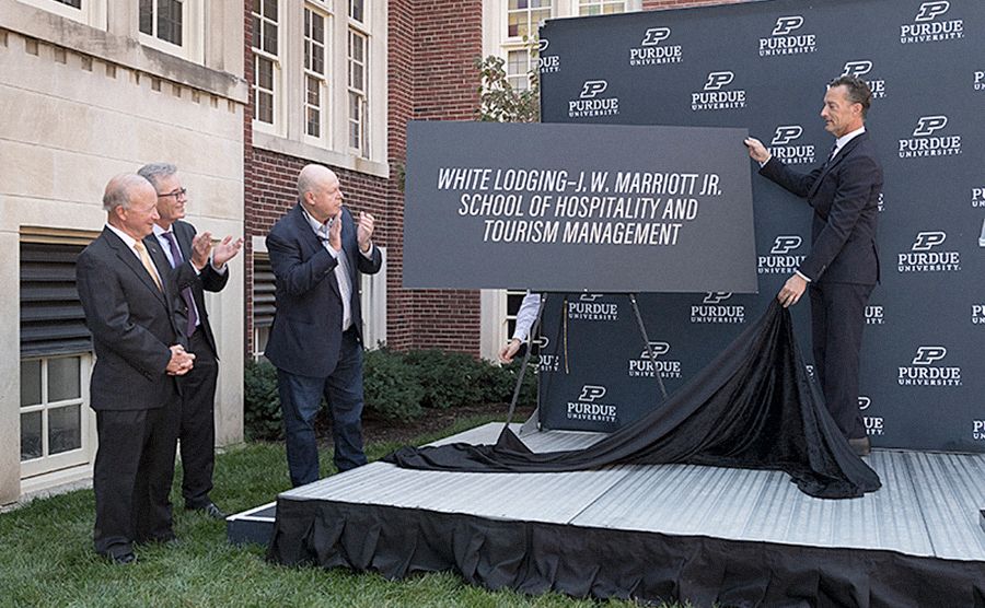 The image shows people by a sign that says "White Lodging-J.W. Marriott Jr. School of Hospitality and Tourism Management"