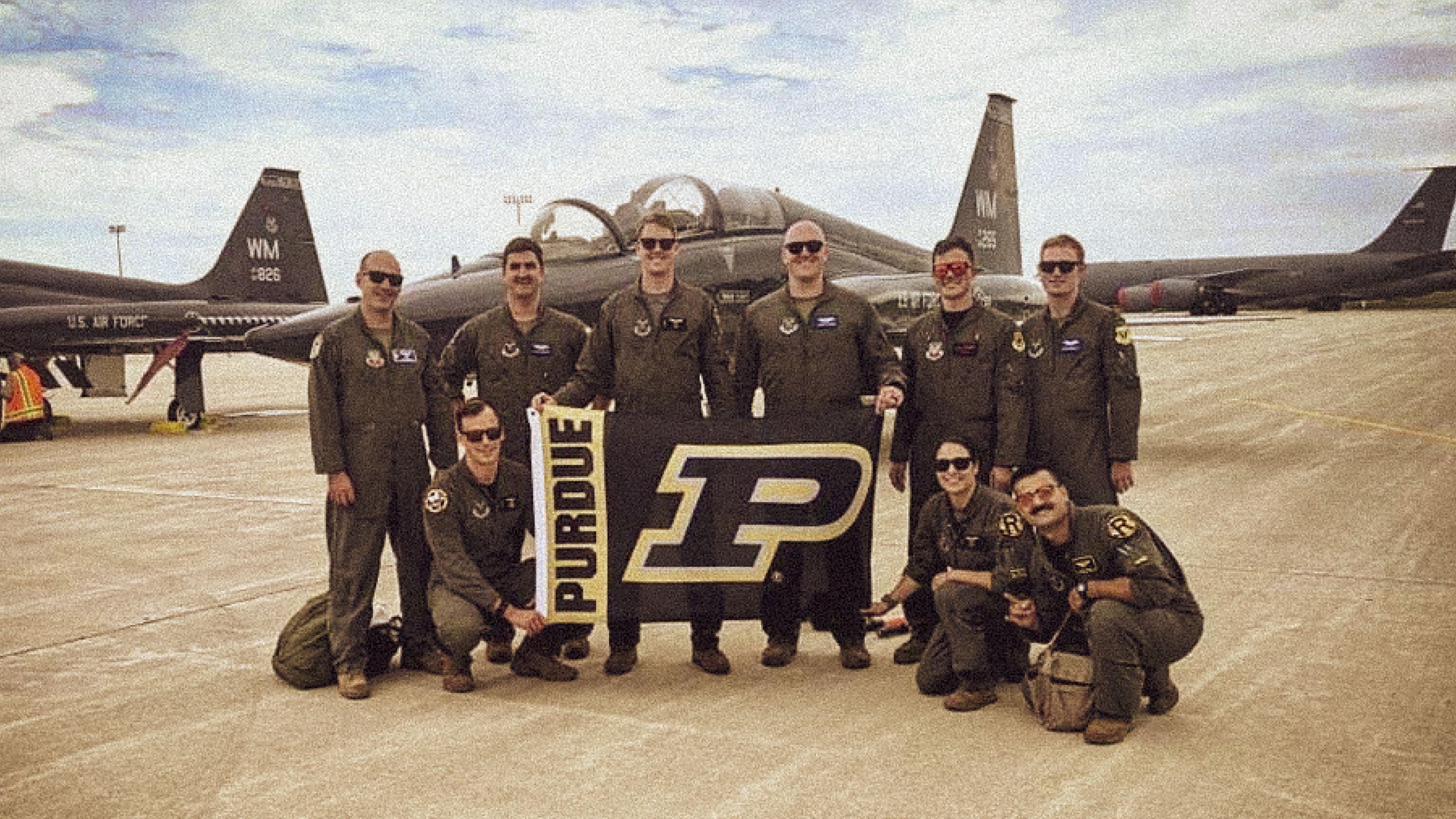 The image shows Purdue alumni and Air Force members with Purdue flags