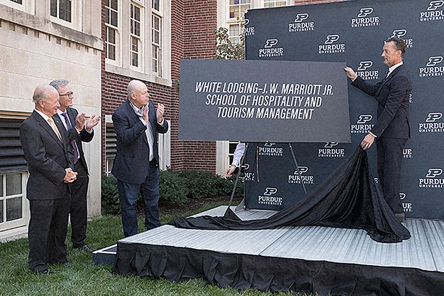 The image shows people by a sign that says "White Lodging-J.W. Marriott Jr. School of Hospitality and Tourism Management"