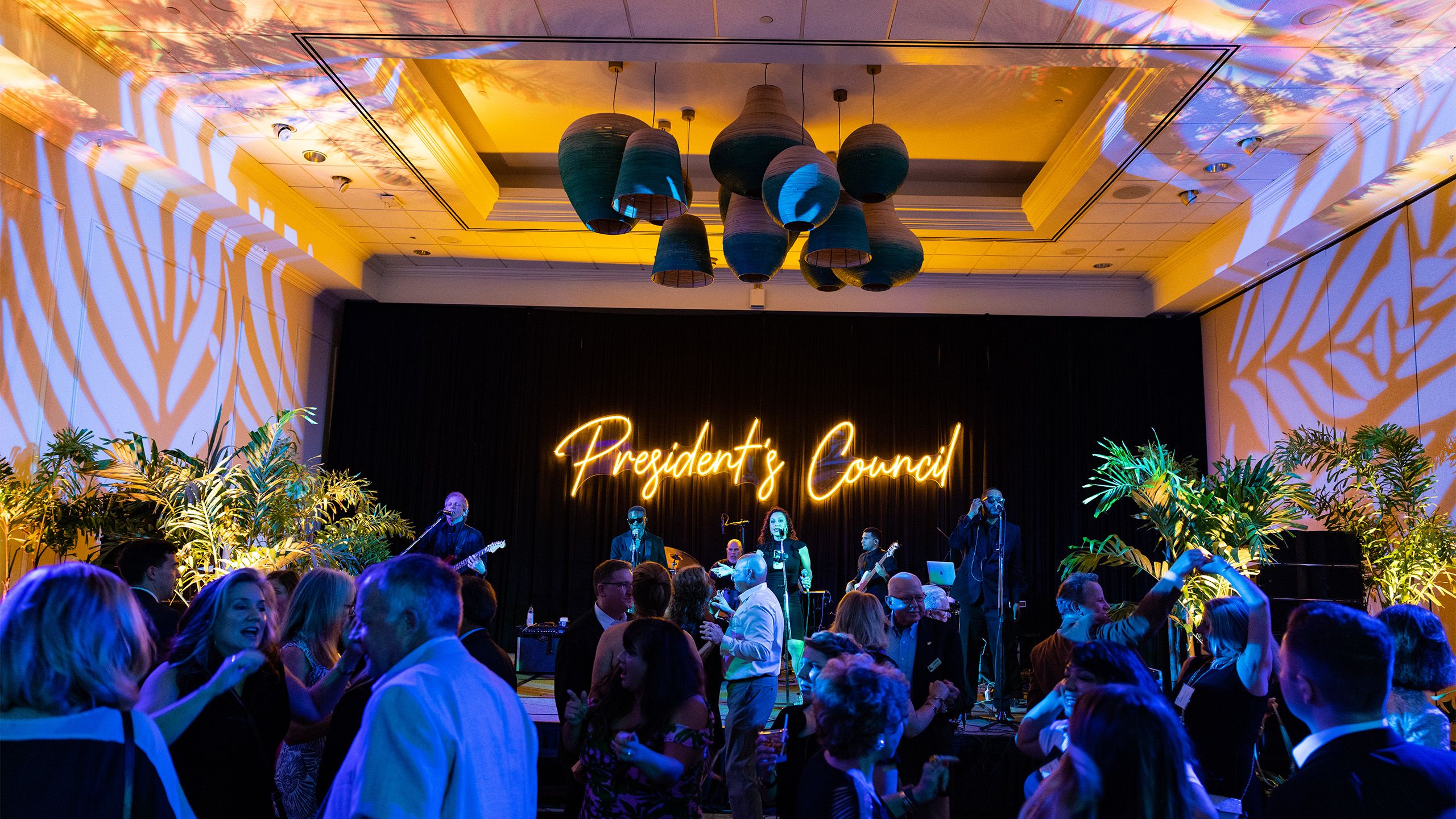 People dance in front of a stage that says "President's Council" in neon lights