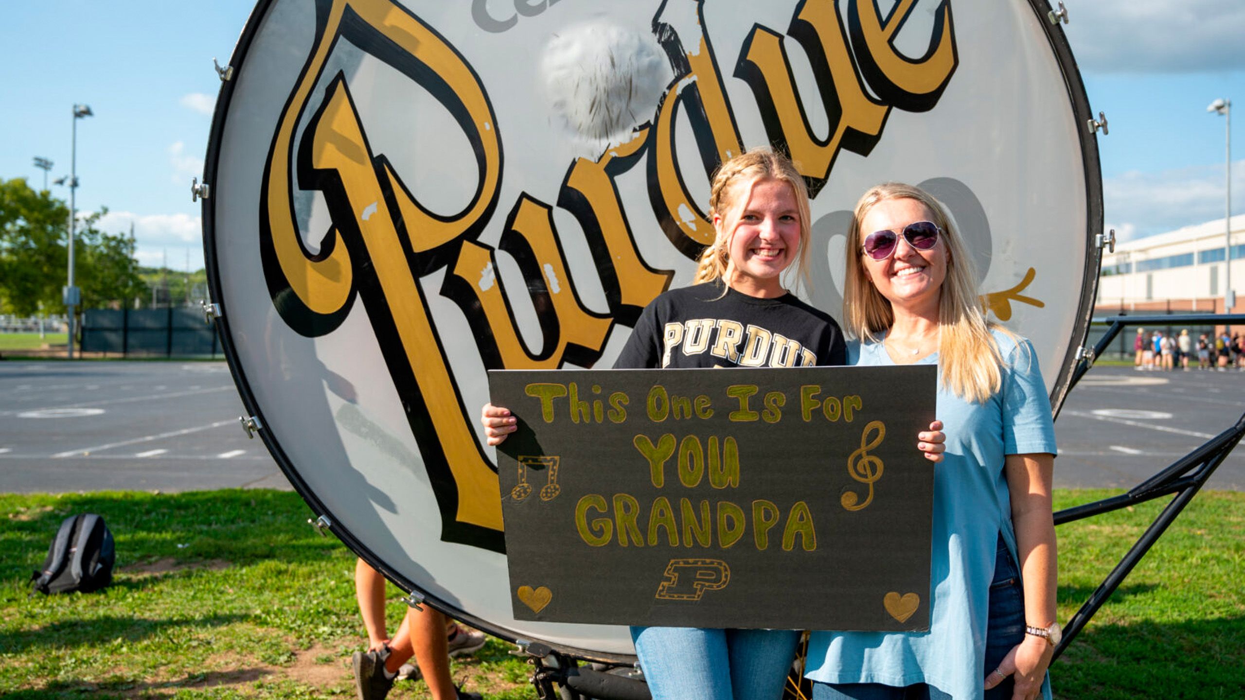 Two women stand in front of the Big Bass Drum with a sign that says "This one is for you Grandpa"