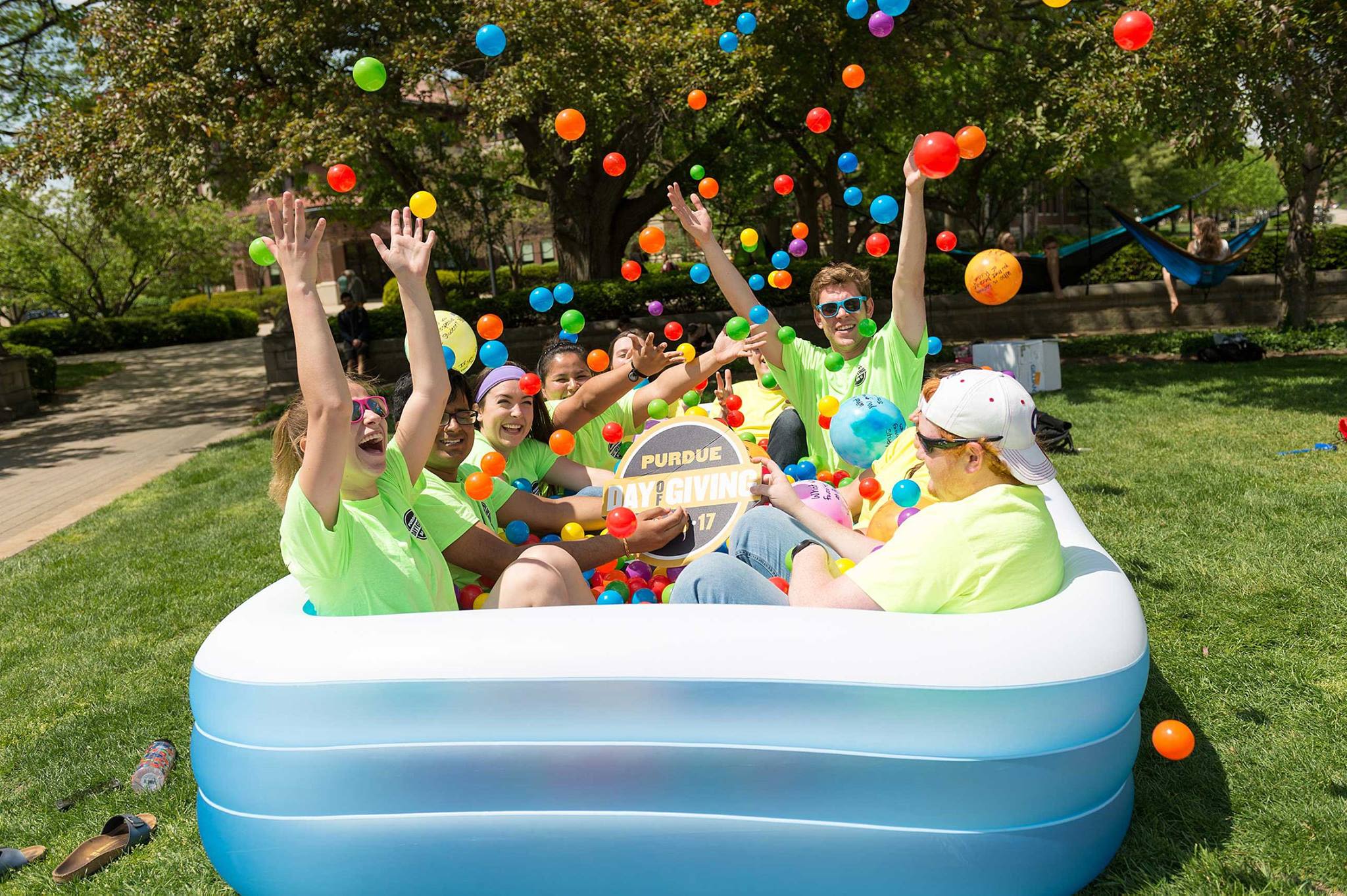 Students sit in an inflatable pool outside and throw plastic balls in the air