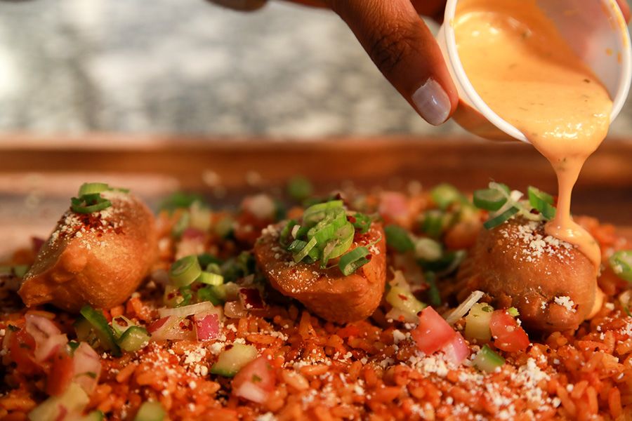A hand pouring sauce over a latin dish