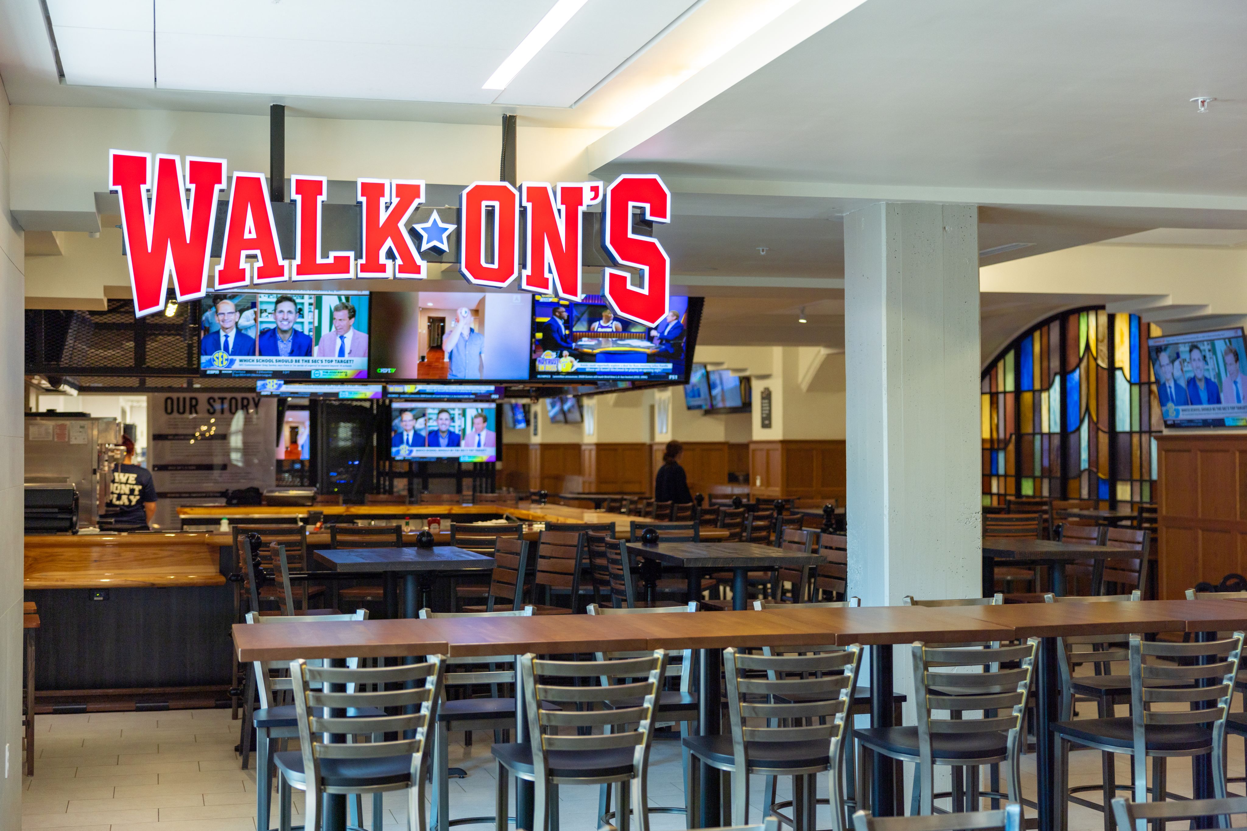 Large lit sign displaying "Walk-On's" logo at the entrance of the restaurant. Seating and TVs are visible in the background