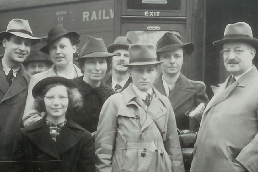 The black-and-white image shows a group of people in trench coats and hats